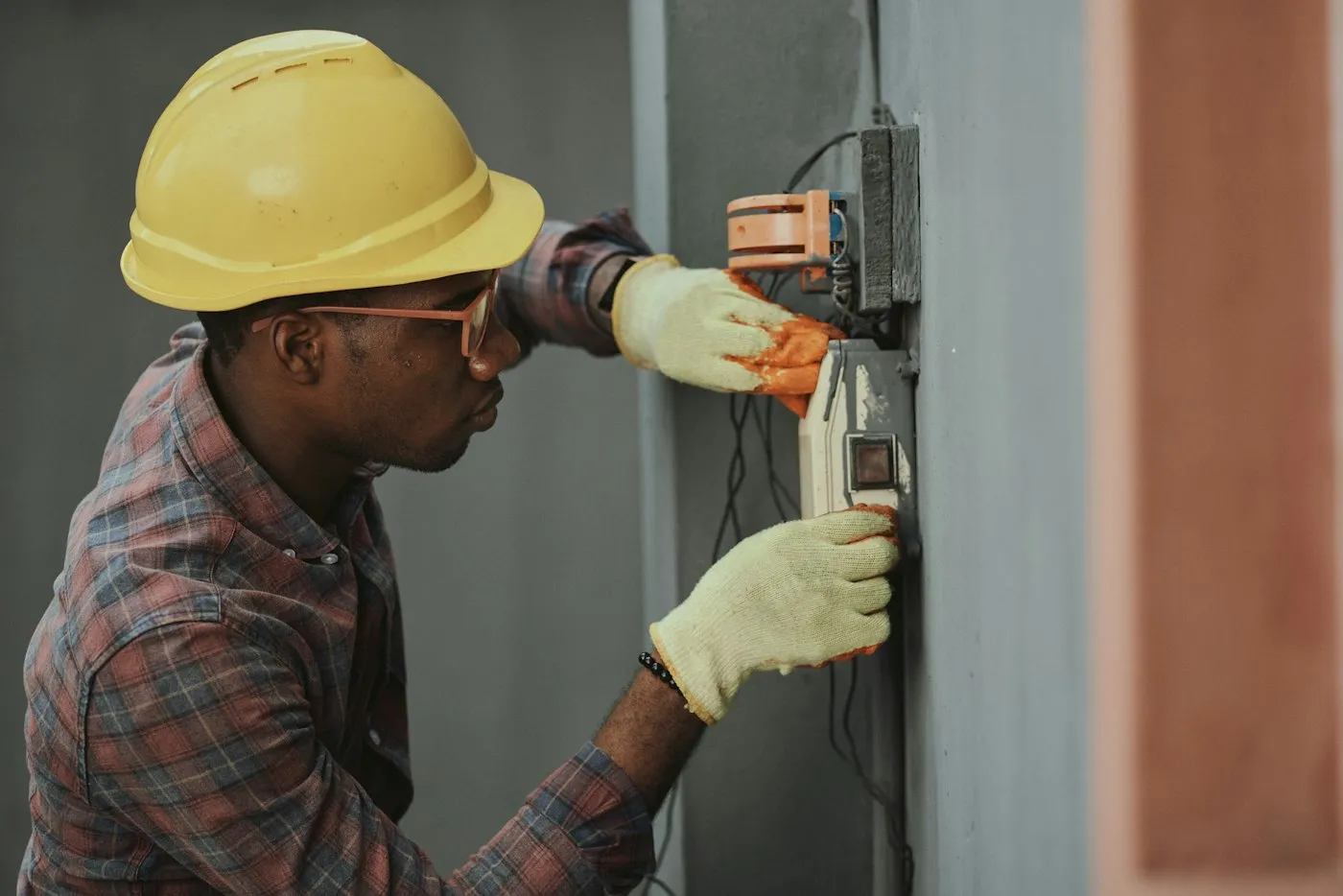 A tradesperson in a hard hat and gloves working on wall wiring (stock photo, provisional)